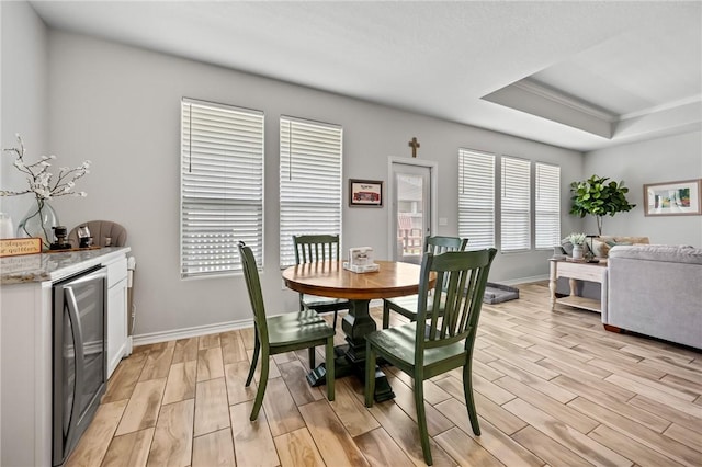 dining space with beverage cooler, a raised ceiling, light wood finished floors, and baseboards