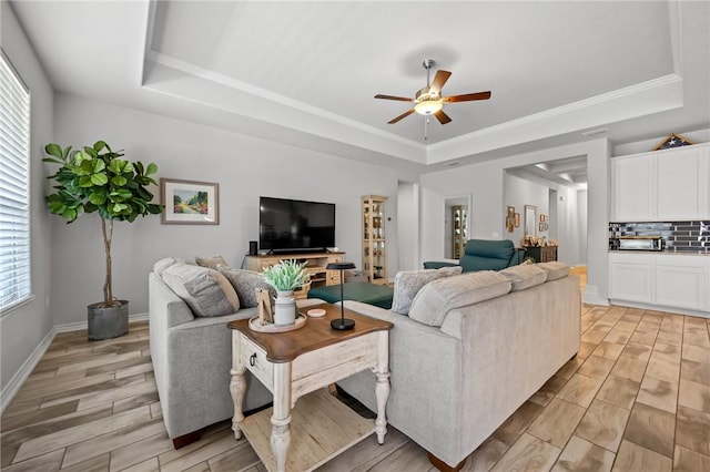 living room featuring a ceiling fan, light wood-type flooring, a toaster, baseboards, and a tray ceiling