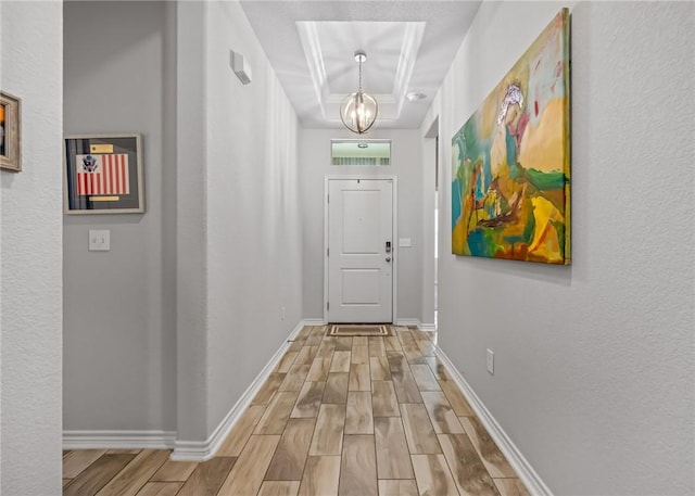 hall with baseboards, light wood-style flooring, a chandelier, and a tray ceiling