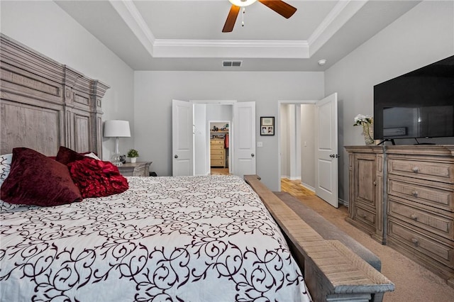 bedroom with visible vents, ornamental molding, light carpet, ceiling fan, and a tray ceiling