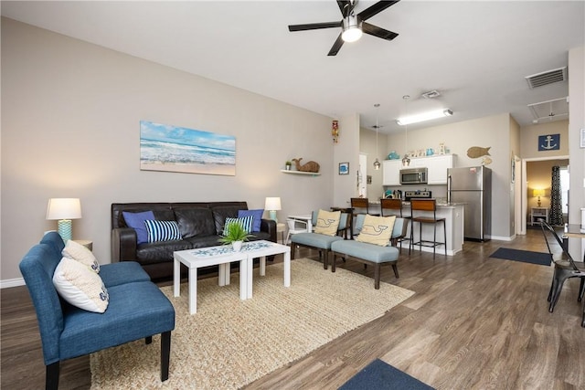 living room with dark wood-style flooring, visible vents, attic access, ceiling fan, and baseboards