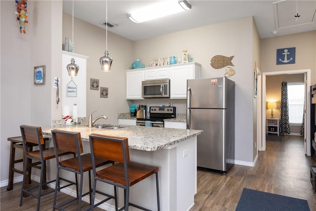 kitchen with dark wood-style floors, a breakfast bar area, appliances with stainless steel finishes, a sink, and a peninsula