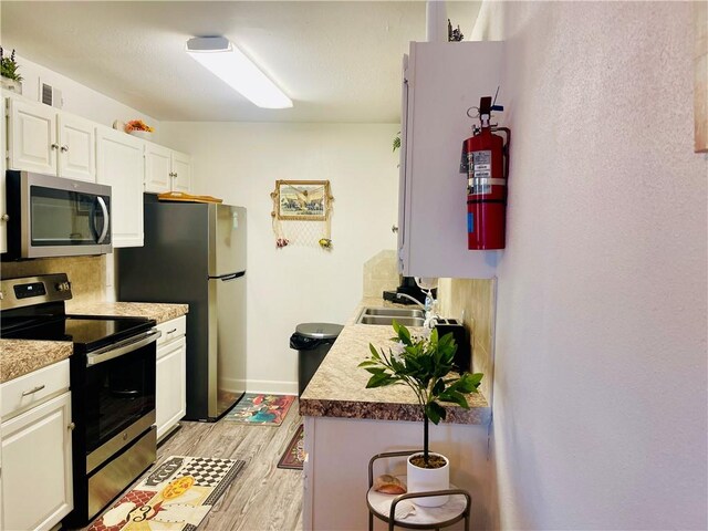 kitchen featuring sink, tasteful backsplash, light hardwood / wood-style floors, white cabinets, and appliances with stainless steel finishes