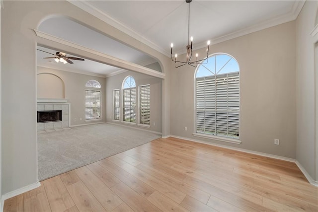 unfurnished living room with crown molding, a tiled fireplace, light wood-type flooring, and ceiling fan with notable chandelier