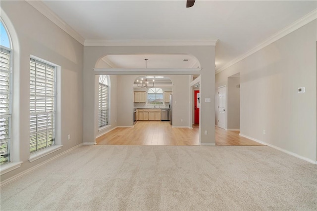 unfurnished living room featuring light carpet, a wealth of natural light, and crown molding