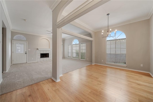 unfurnished living room featuring ceiling fan with notable chandelier, light colored carpet, crown molding, and a tile fireplace