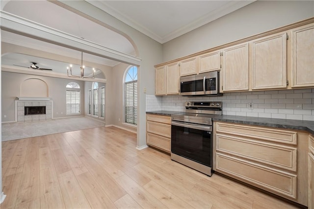 kitchen featuring appliances with stainless steel finishes, backsplash, a tile fireplace, ceiling fan with notable chandelier, and light hardwood / wood-style floors