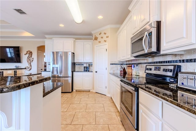 kitchen featuring decorative backsplash, appliances with stainless steel finishes, ornamental molding, dark stone countertops, and white cabinets