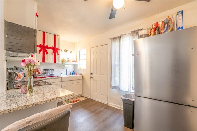 kitchen featuring sink, white cabinetry, dark wood-type flooring, light stone countertops, and stainless steel fridge