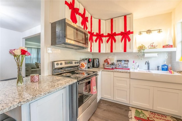 kitchen featuring appliances with stainless steel finishes, wood-type flooring, white cabinets, light stone counters, and sink