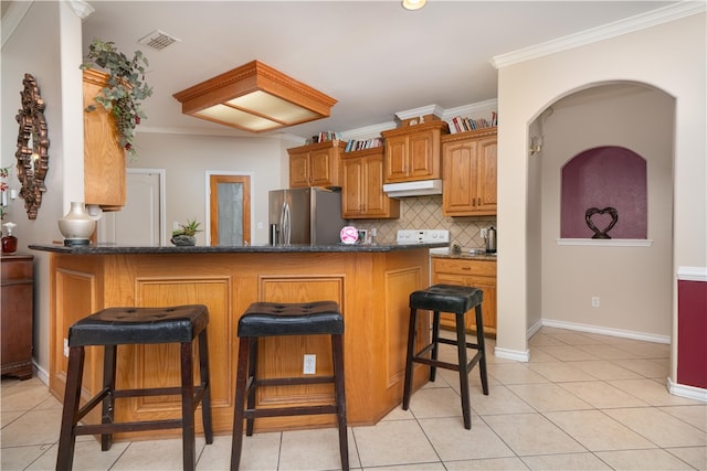 kitchen with ornamental molding, light tile patterned flooring, stainless steel fridge, decorative backsplash, and a breakfast bar