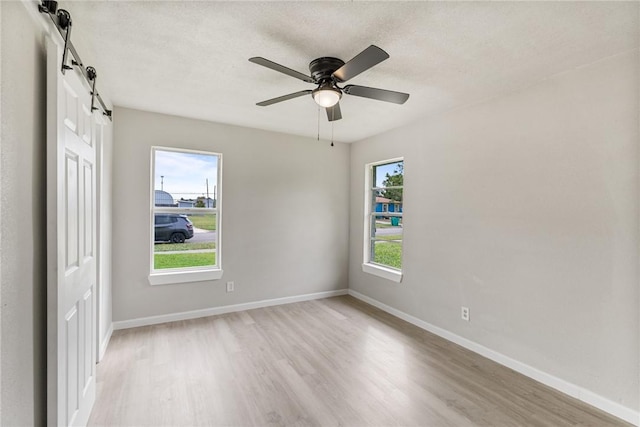 spare room with a textured ceiling, a barn door, light hardwood / wood-style floors, and ceiling fan