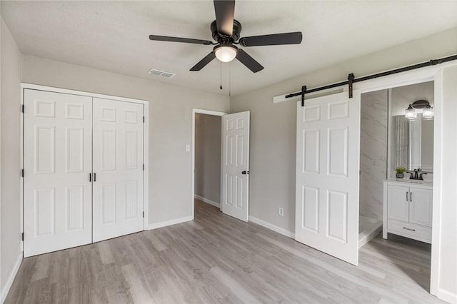 unfurnished bedroom with ensuite bathroom, ceiling fan, sink, a barn door, and light hardwood / wood-style flooring