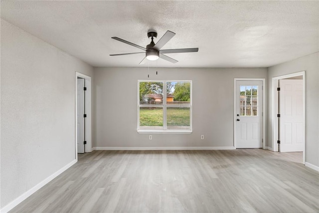 empty room featuring a textured ceiling, light wood-type flooring, a wealth of natural light, and ceiling fan