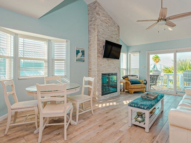 living room featuring high vaulted ceiling, a stone fireplace, light hardwood / wood-style floors, and ceiling fan