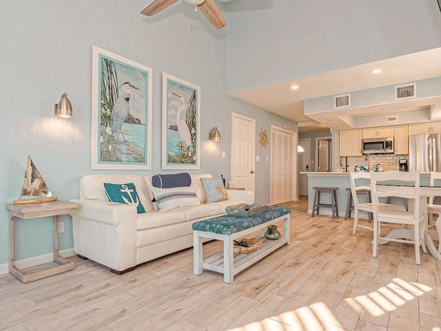 living room featuring ceiling fan, light hardwood / wood-style flooring, and a high ceiling