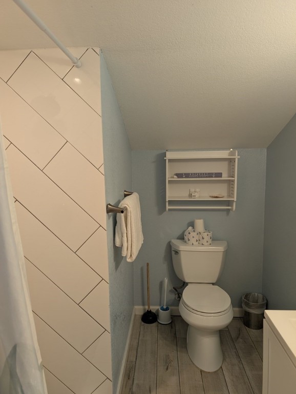 bathroom with toilet, vaulted ceiling, a textured ceiling, vanity, and hardwood / wood-style flooring