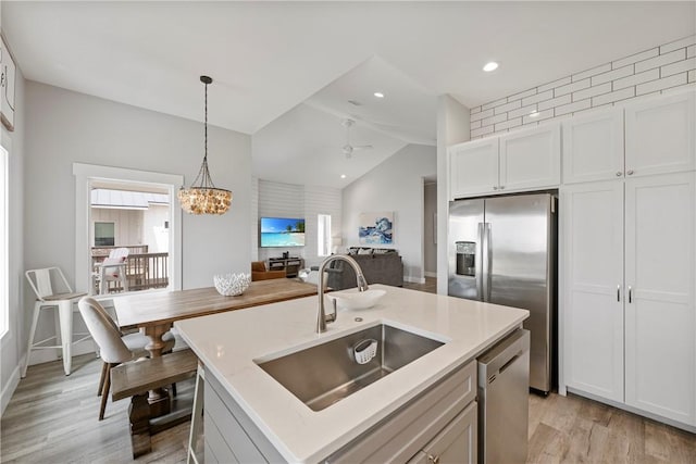 kitchen with a sink, appliances with stainless steel finishes, lofted ceiling, light wood-style floors, and decorative light fixtures