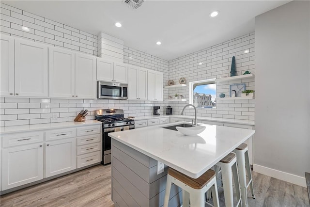 kitchen with stainless steel appliances, open shelves, a sink, light countertops, and white cabinetry