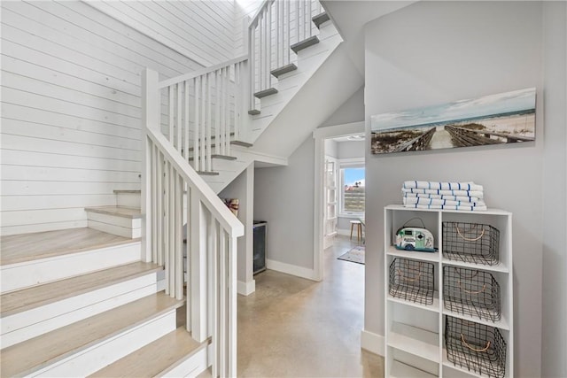 staircase featuring concrete floors, baseboards, and wood walls