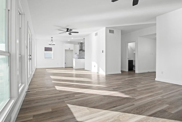 unfurnished living room with ceiling fan with notable chandelier, wood finished floors, and visible vents