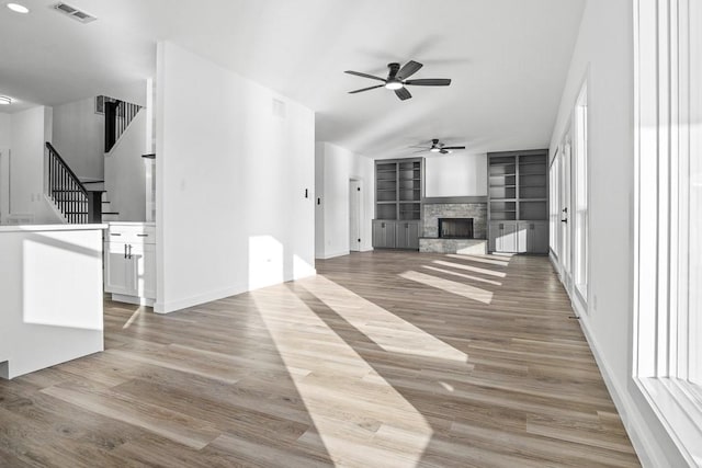 unfurnished living room with visible vents, wood finished floors, stairs, built in shelves, and a fireplace