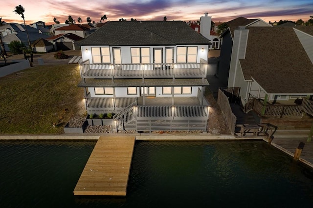 back of property at dusk with a balcony, roof with shingles, a residential view, a chimney, and stairway