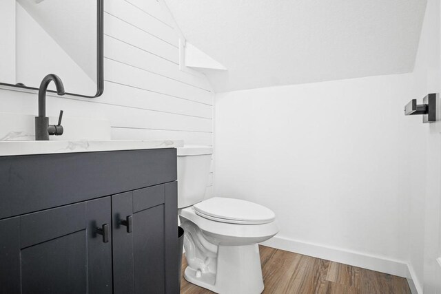 half bathroom featuring baseboards, toilet, lofted ceiling, wood finished floors, and vanity