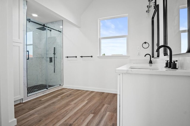bathroom with wood finished floors, a stall shower, baseboards, vaulted ceiling, and double vanity