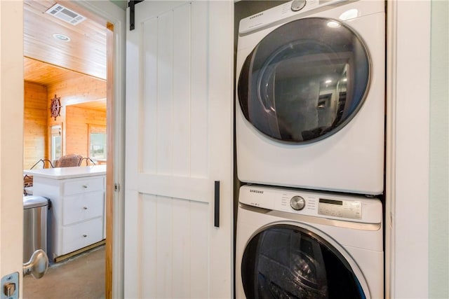 washroom with visible vents, laundry area, stacked washer / drying machine, wood walls, and a barn door