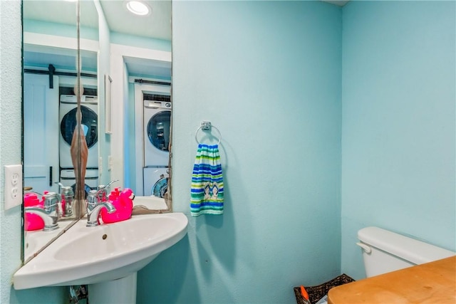 bathroom featuring toilet, stacked washer and clothes dryer, and a sink