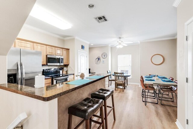 kitchen featuring visible vents, a kitchen breakfast bar, stainless steel appliances, and light brown cabinetry