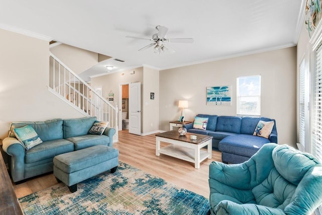 living area with a ceiling fan, baseboards, stairway, light wood-type flooring, and crown molding