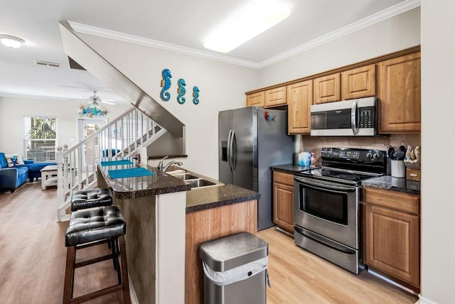 kitchen featuring light wood finished floors, appliances with stainless steel finishes, ornamental molding, a sink, and a kitchen breakfast bar