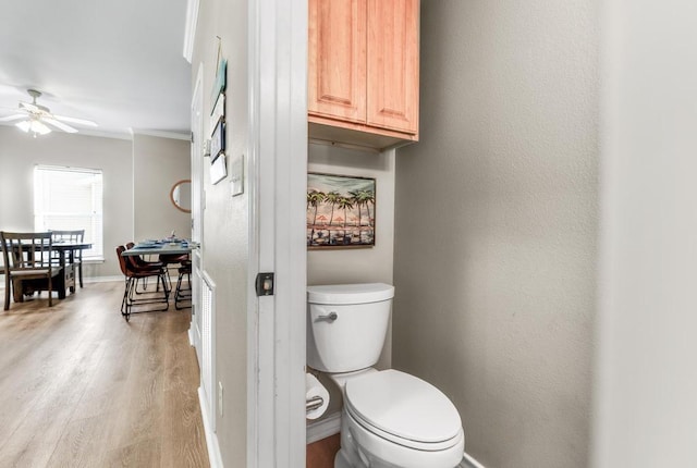 bathroom featuring baseboards, toilet, ceiling fan, wood finished floors, and crown molding