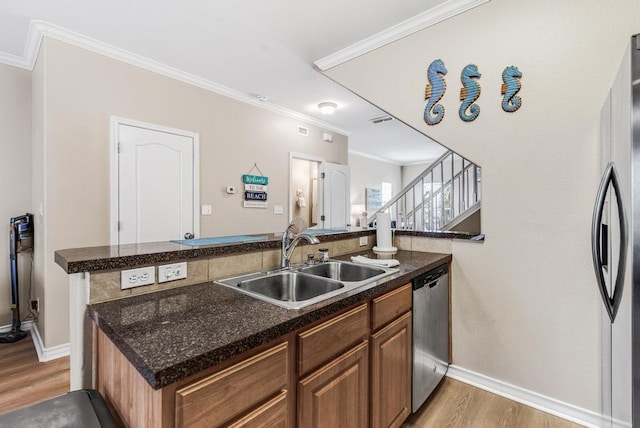 kitchen featuring light wood finished floors, appliances with stainless steel finishes, a sink, and crown molding