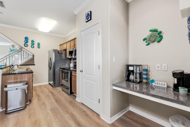 kitchen featuring appliances with stainless steel finishes, light wood-type flooring, crown molding, and built in desk