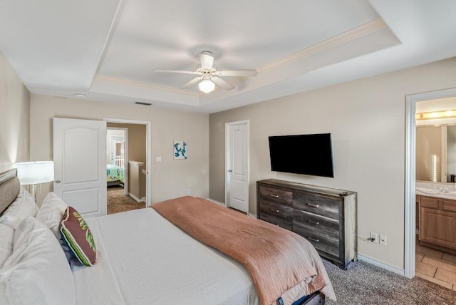 bedroom with light carpet, ceiling fan, a raised ceiling, and connected bathroom