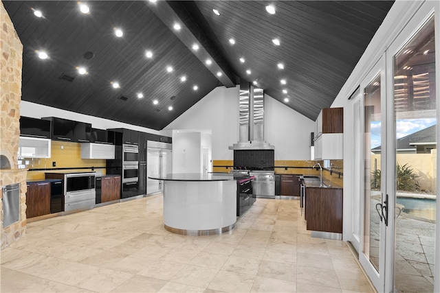 kitchen with a kitchen island, wall chimney range hood, appliances with stainless steel finishes, high vaulted ceiling, and decorative backsplash