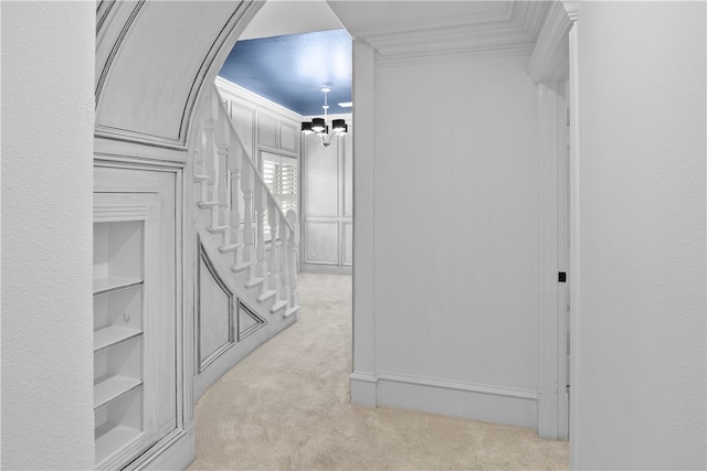 hallway featuring light carpet, crown molding, and an inviting chandelier