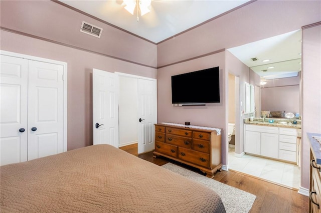 bedroom with ensuite bath, a sink, visible vents, light wood-type flooring, and two closets