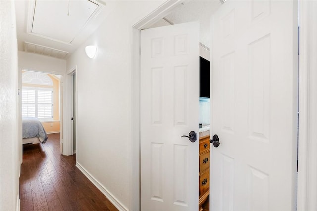 hall with attic access, baseboards, and dark wood-style floors