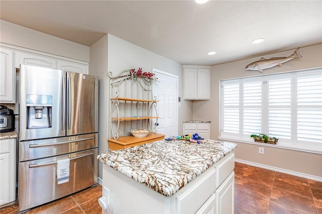 kitchen with stainless steel refrigerator with ice dispenser, white cabinets, a kitchen island, light stone countertops, and baseboards