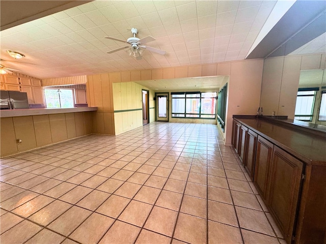 kitchen featuring black refrigerator, ceiling fan, light tile patterned flooring, and wood walls