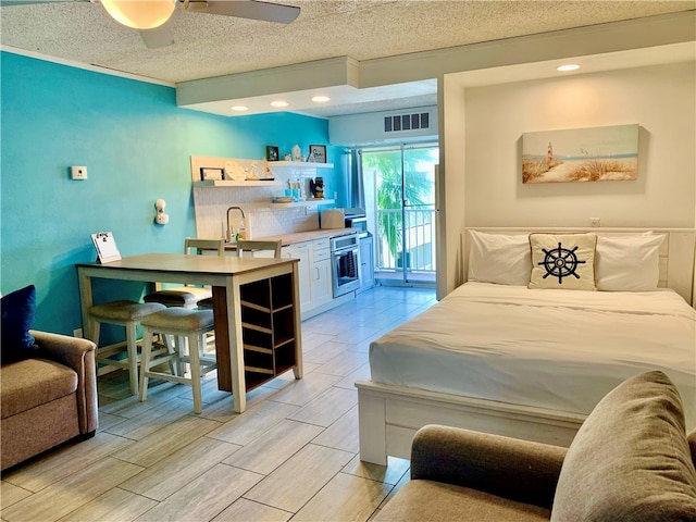 bedroom featuring light hardwood / wood-style floors, sink, ceiling fan, access to exterior, and a textured ceiling