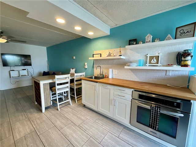 kitchen with sink, butcher block counters, white cabinetry, decorative backsplash, and stainless steel oven