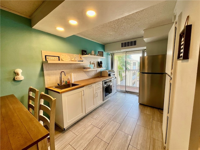 kitchen featuring butcher block counters, sink, white cabinetry, appliances with stainless steel finishes, and backsplash