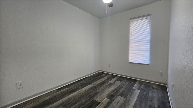 spare room featuring a textured wall, dark wood-style flooring, ceiling fan, and baseboards