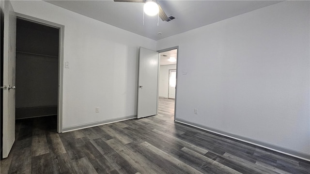 unfurnished bedroom with a ceiling fan, baseboards, a walk in closet, and dark wood finished floors