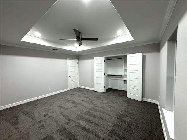 unfurnished bedroom with a raised ceiling, crown molding, ceiling fan, and dark colored carpet